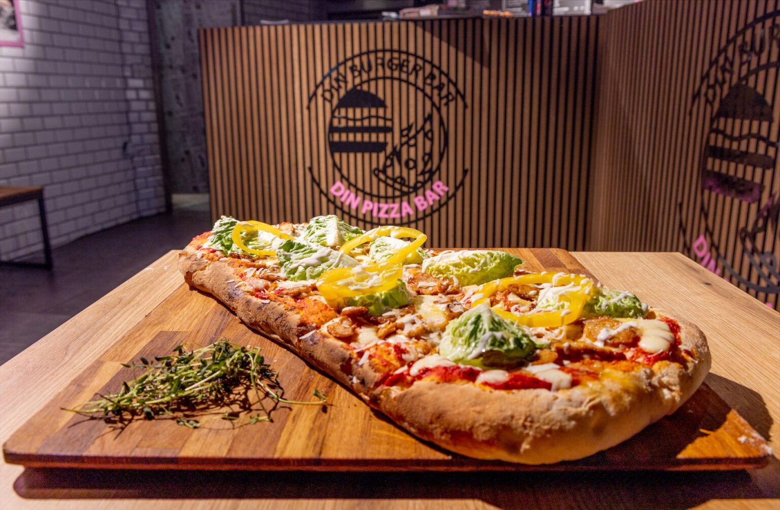 Rektangulær pizza med salat og paprika på træplade.