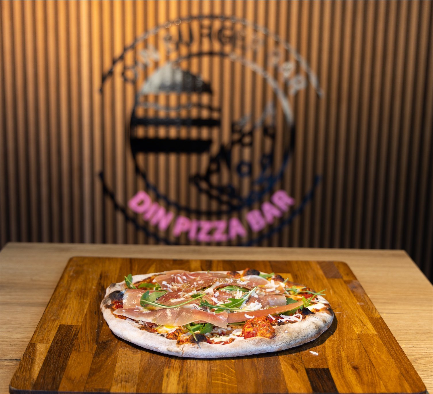 Pizza med parmaskinke og rucola på træbræt.